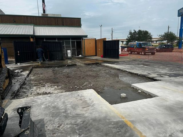 Crumbling concrete lot beside a small building, with broken pavement and construction equipment in the background.