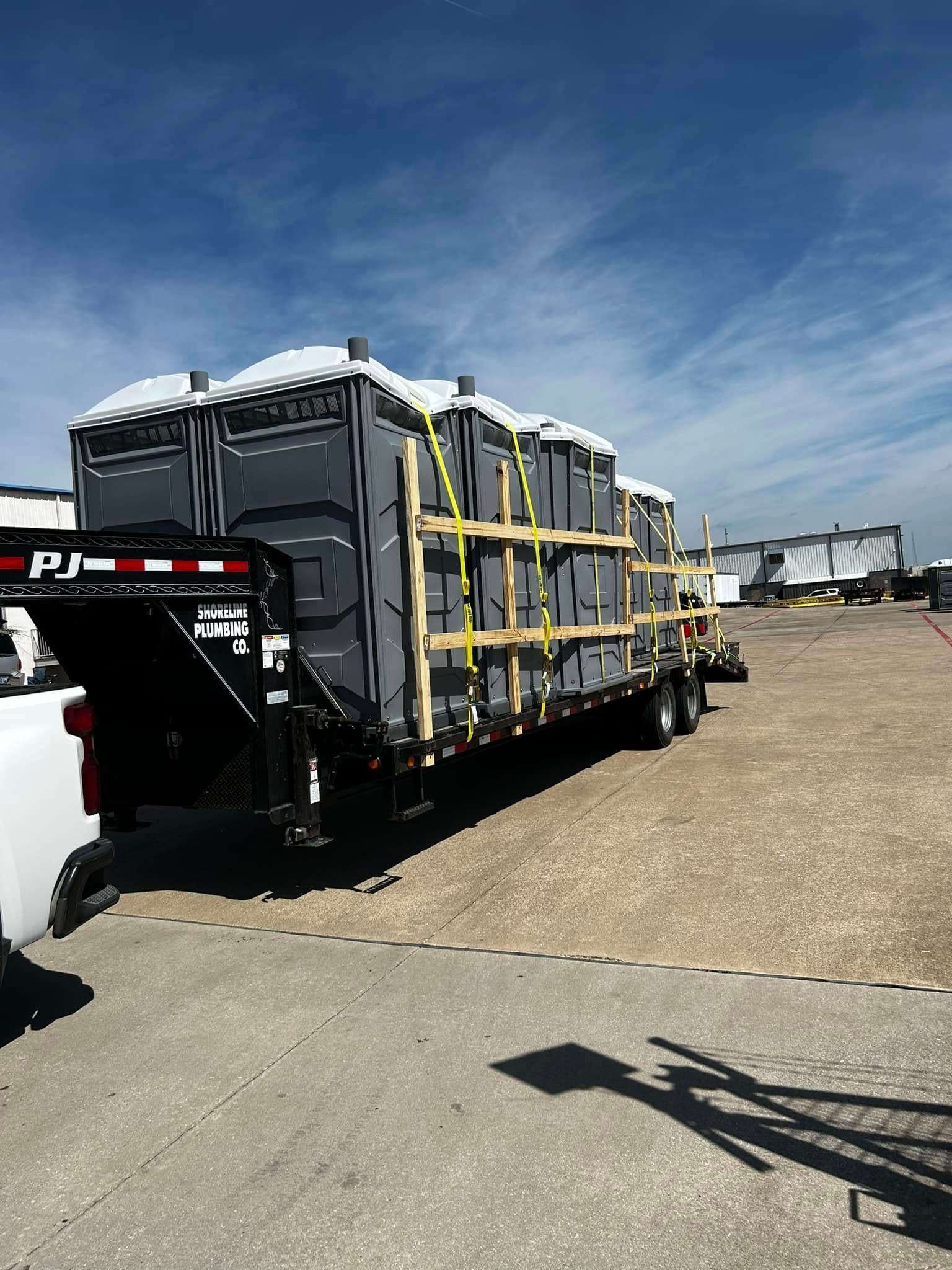 Black flatbed trailer loaded with wrapped cargo strapped down in a sunny industrial yard