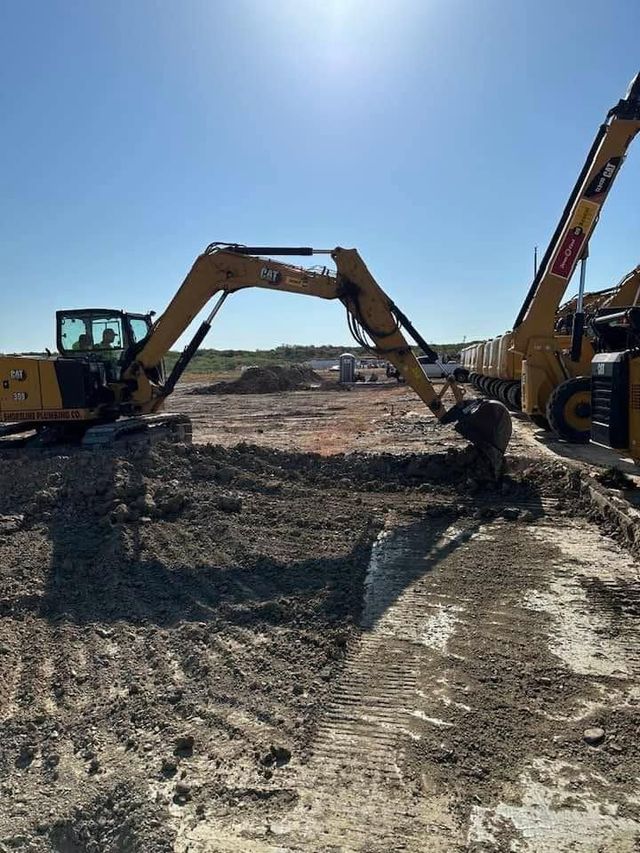 Two excavators digging earth at a construction site under a bright blue sky