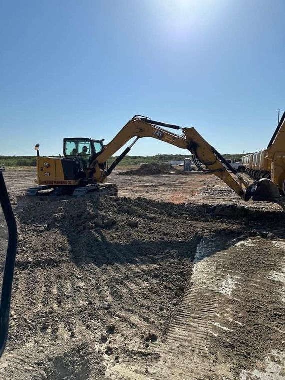 Yellow excavator leveling dirt at a construction site under a clear blue sky