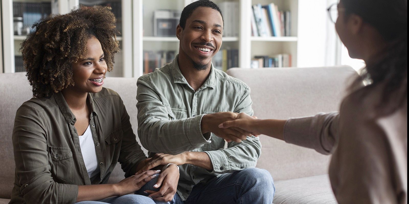 A couple shakes hands with a therapist on a couch in a counseling session. Both parties are smiling.