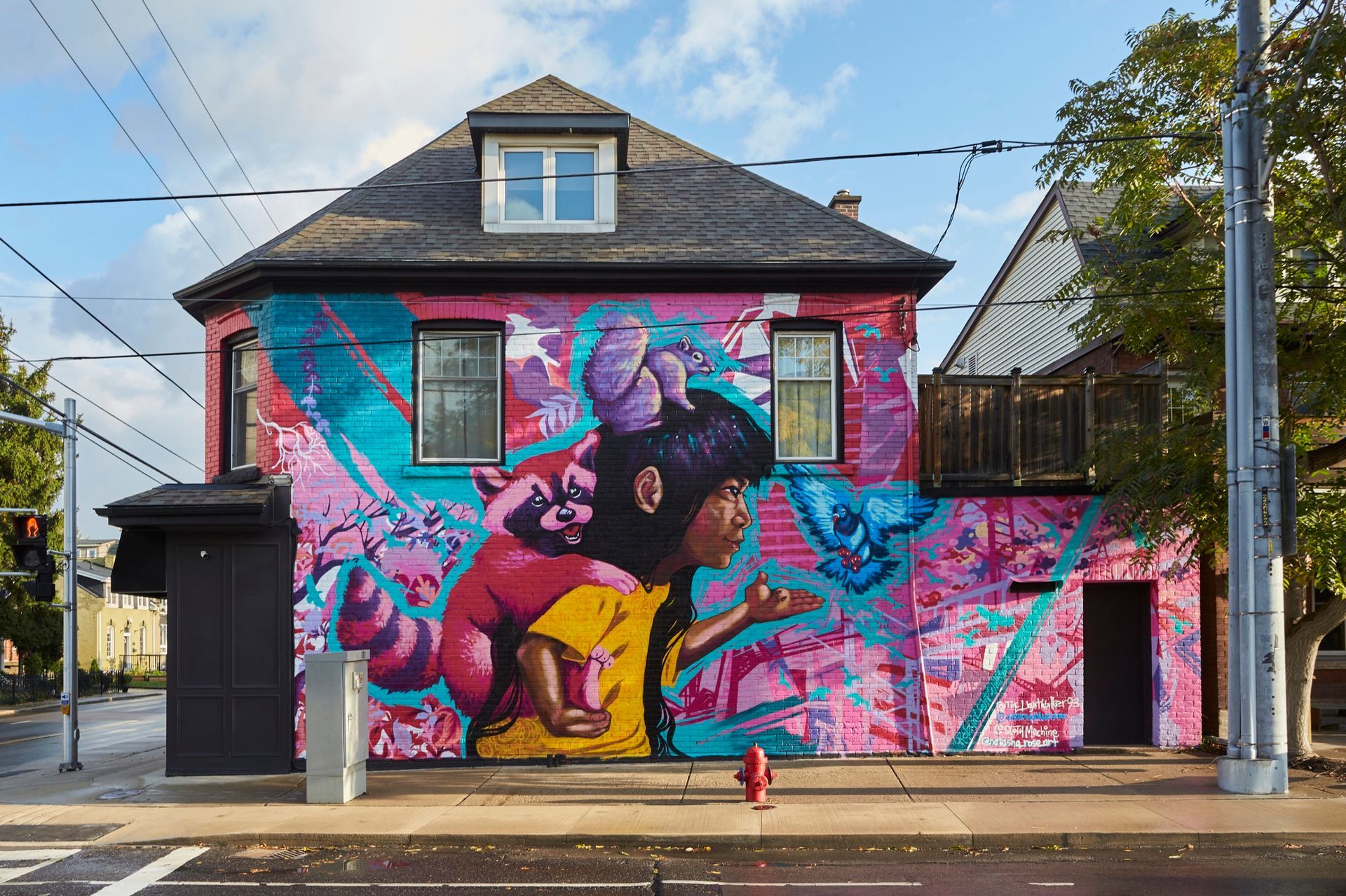 Mural on building front depicts a child blowing bubbles, vibrant pinks, blues, and yellows. Building is on a city street.