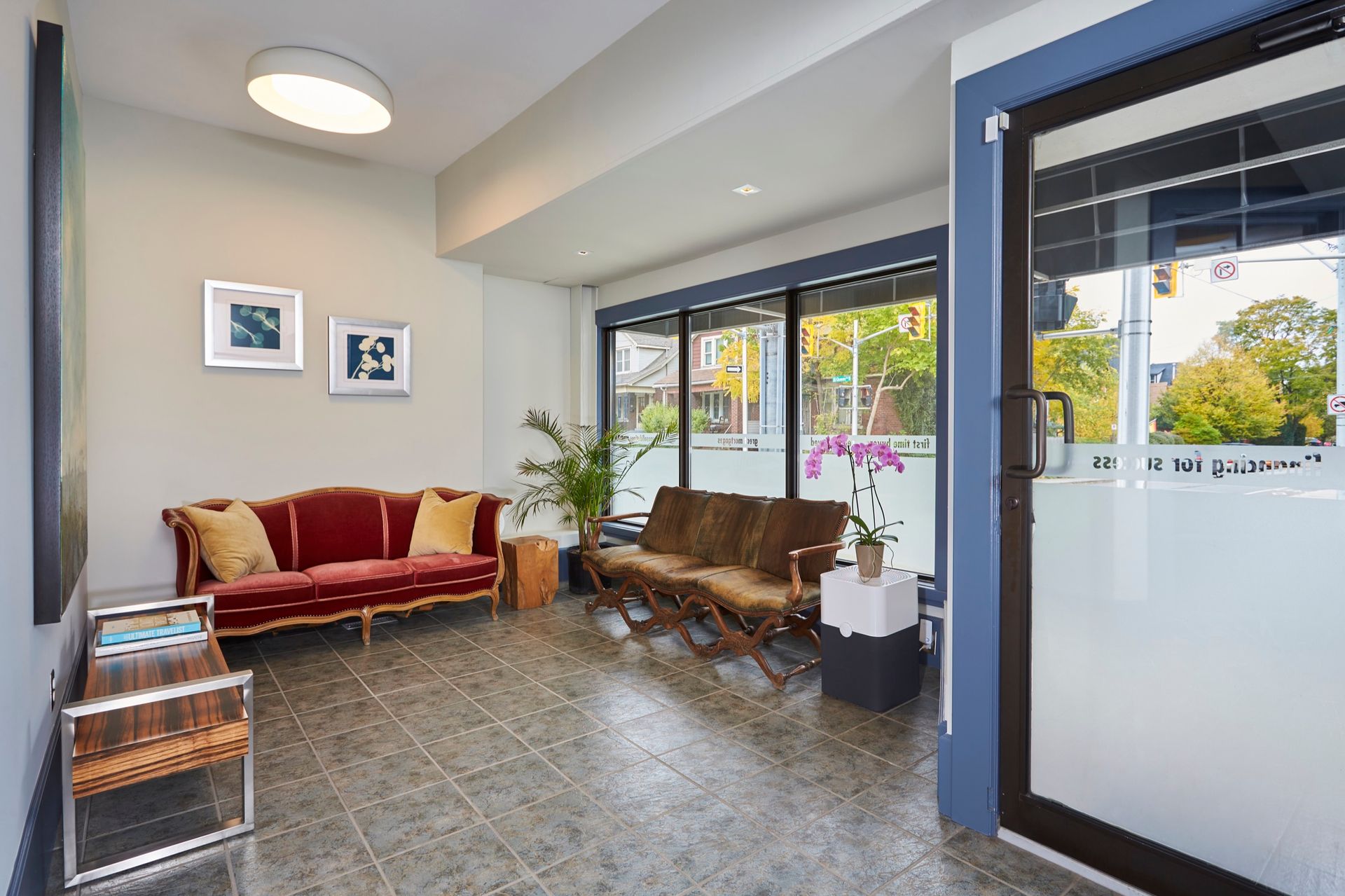 A waiting room with a red couch, two brown chairs, and frosted glass door. 