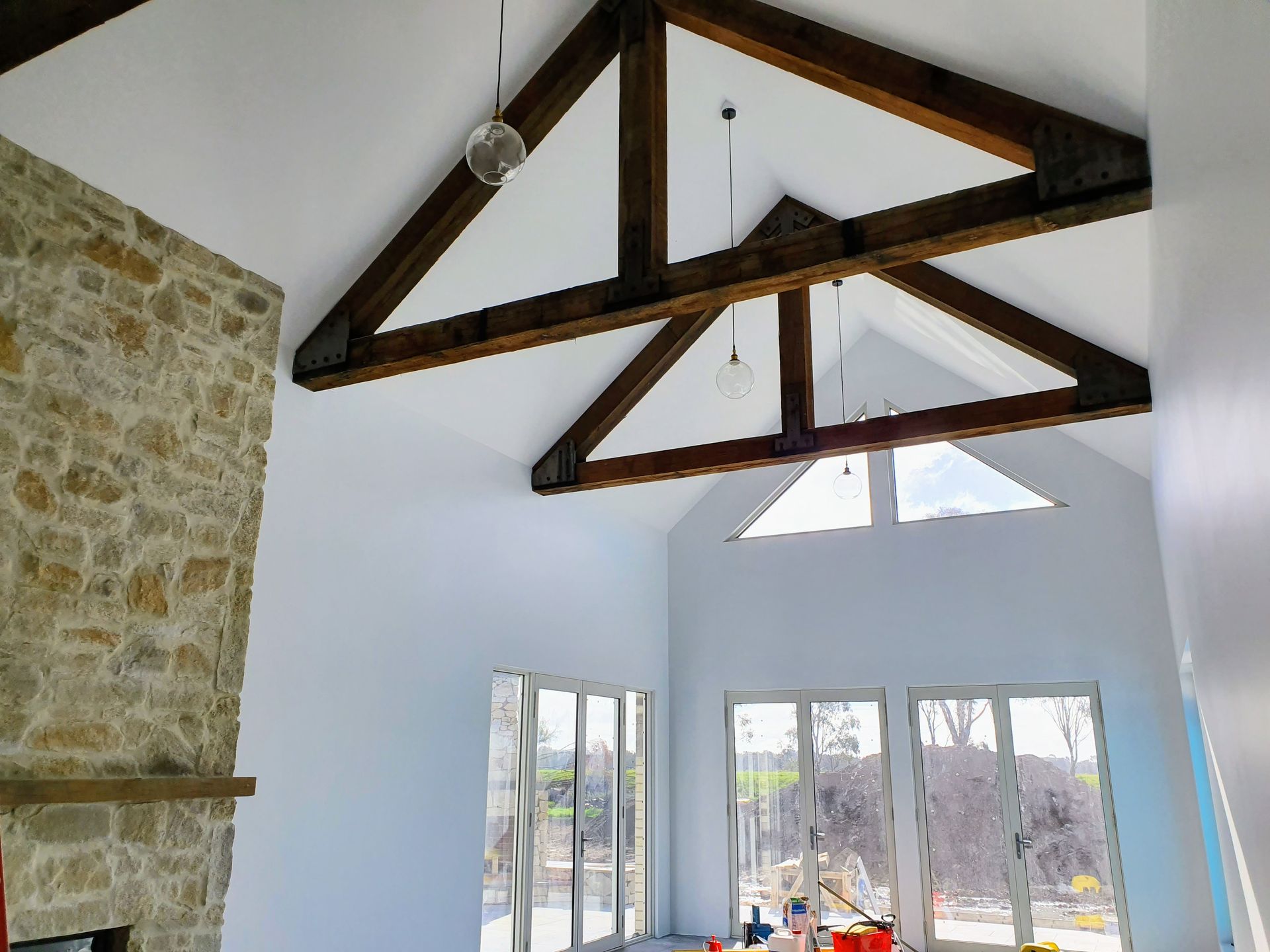 High-ceilinged living room with exposed wooden beams, white walls, stone fireplace, and large windows.
