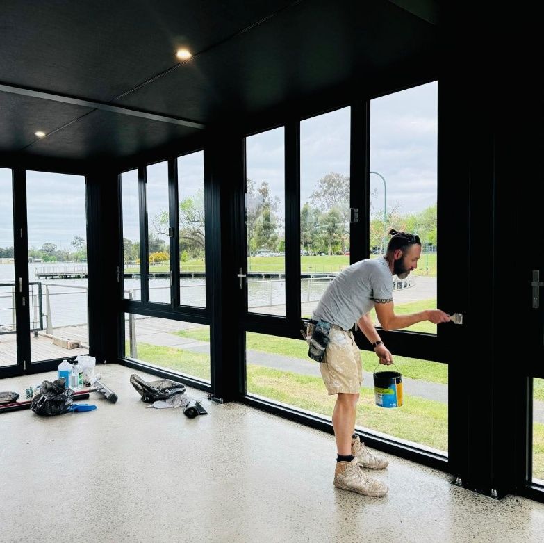 A Man Is Painting A Window In A Room With Lots Of Windows — Crampton Painting & Decorating Pty Ltd In Bendigo, VIC