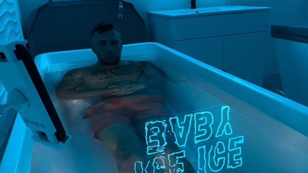 A person sits in an ice bath lit with blue light, with the text 