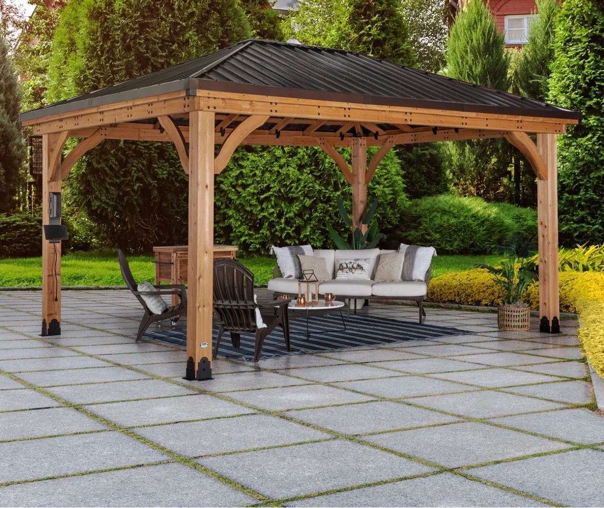 Wooden gazebo with outdoor seating on a stone patio in a landscaped garden
