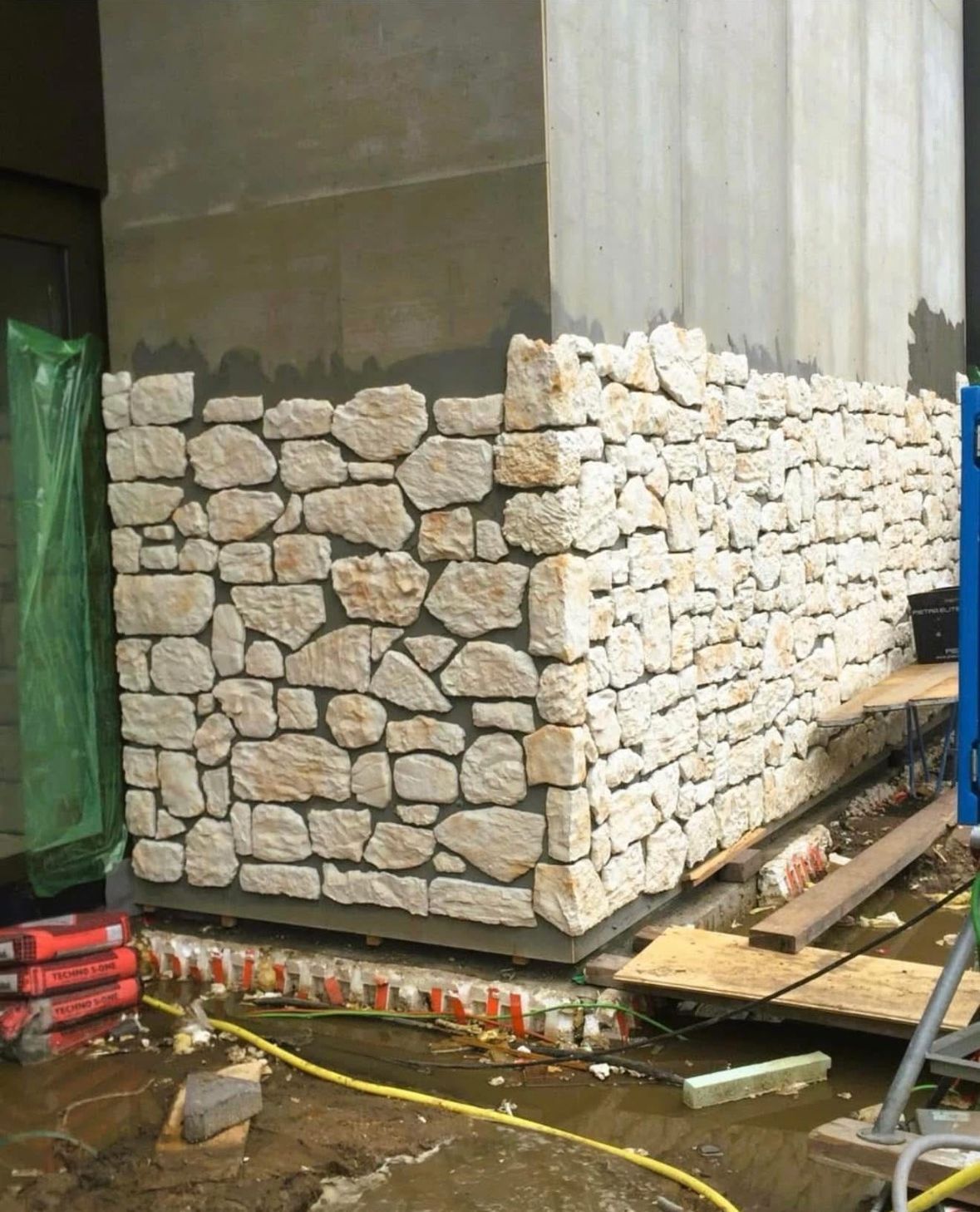 Stone-faced concrete structure at a construction site with scattered materials and wet ground.