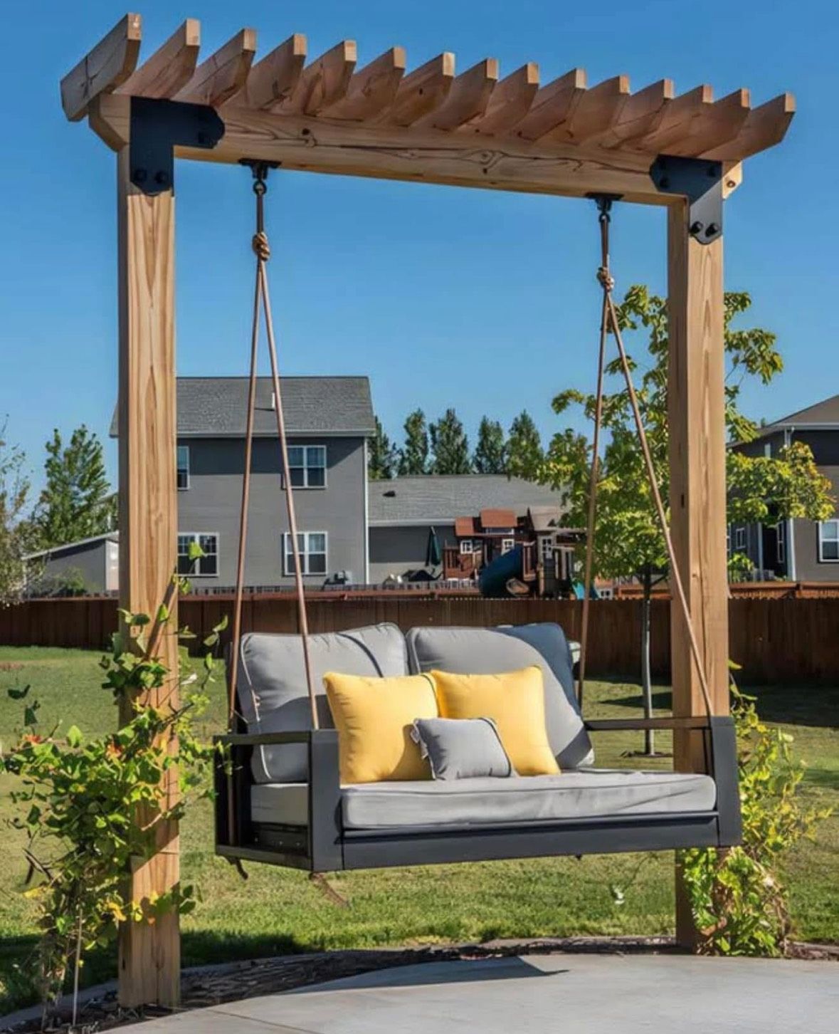 Wooden pergola swing bench with gray cushions and yellow pillows in a sunny backyard