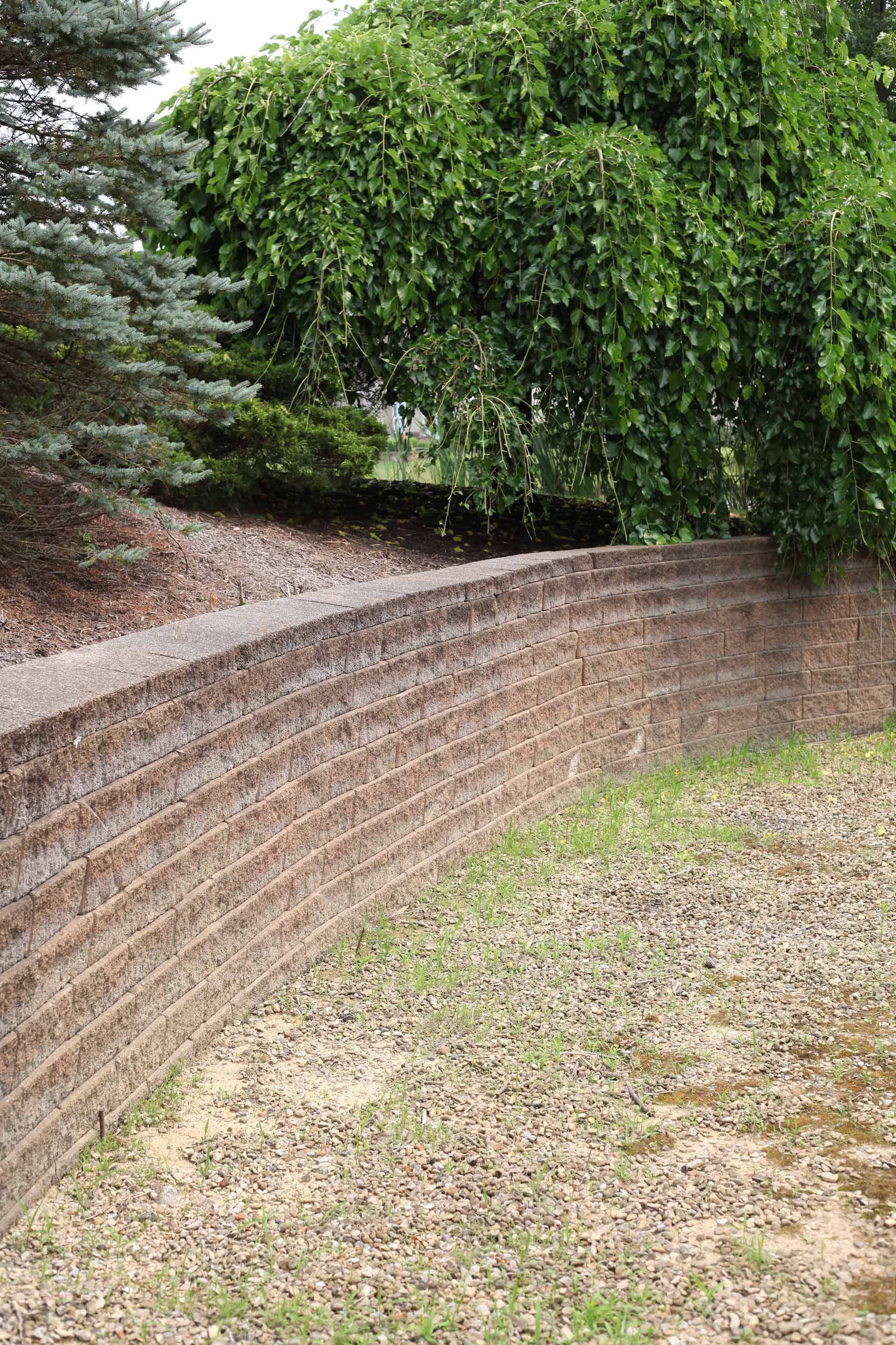 A brick wall in a yard with trees in the background