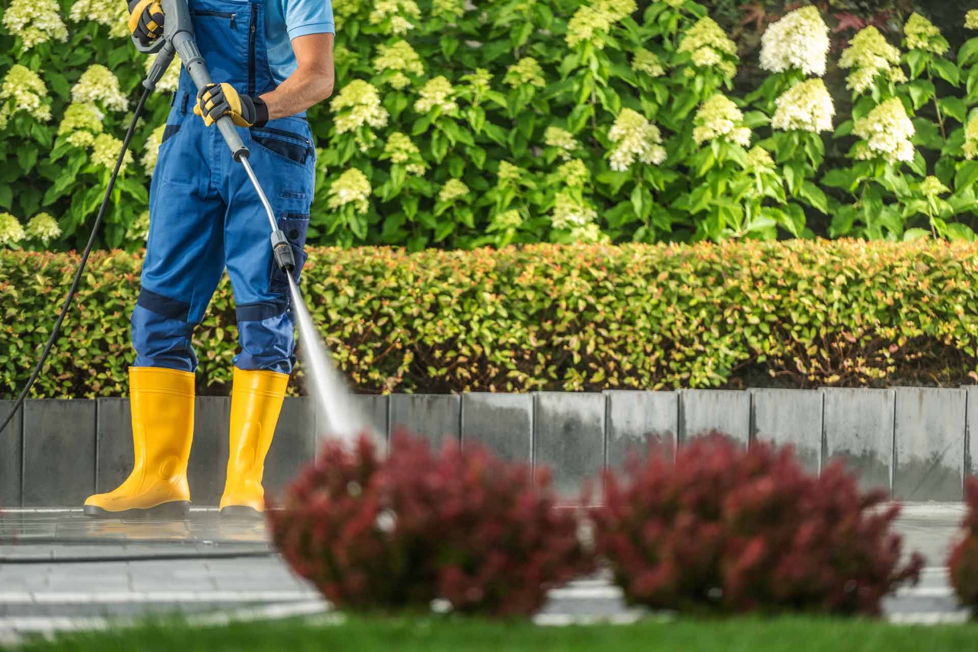 A man is using a high pressure washer to clean a sidewalk