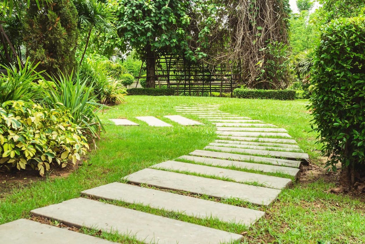 Curved stone stepping path through a lush green garden lawn with shrubs and trees