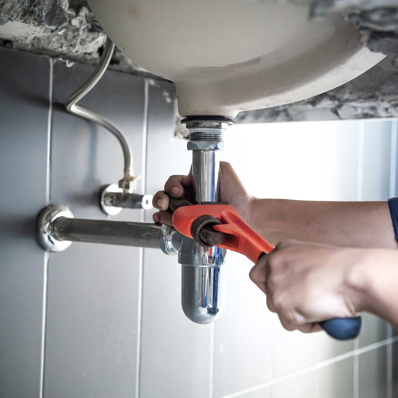 Hands using a red wrench to tighten a bathroom sink drain pipe under the basin