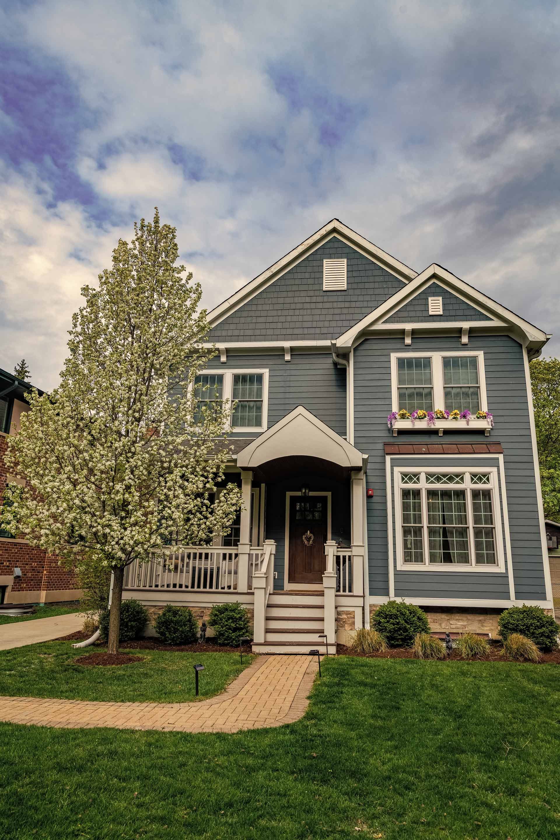 A blue house with a white porch and a tree in front of it