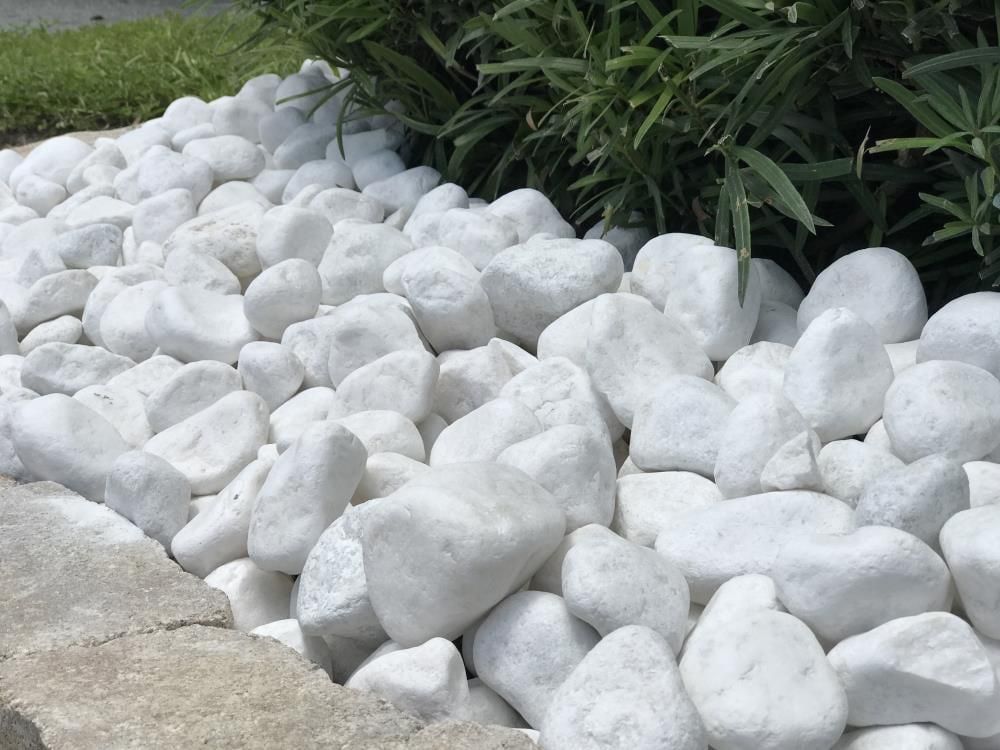 White decorative rocks lining a garden bed beside green plants and a concrete edge