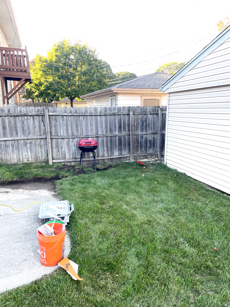 A backyard with a fence, a bucket, and a grill