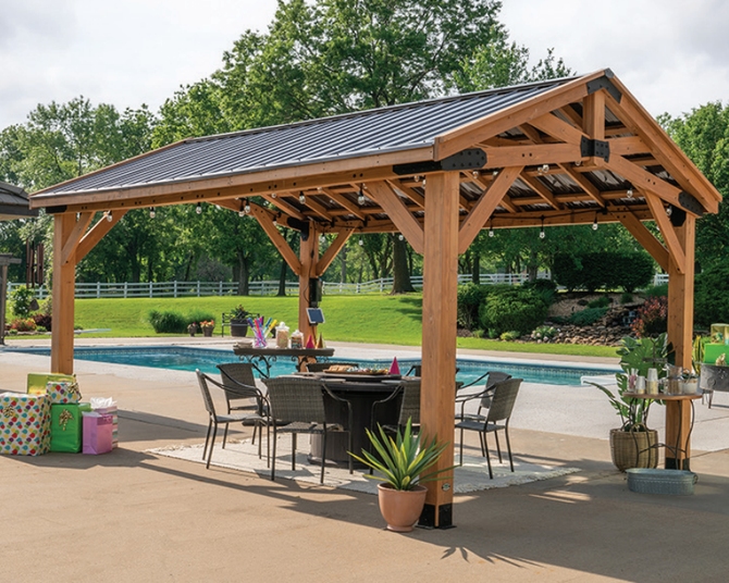Wooden pavilion by a pool with outdoor dining tables, chairs, and potted plants on a sunny day