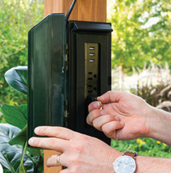 Hands adjusting an outdoor black lockbox on a wooden post in a garden setting