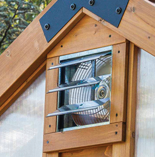 A small vented fan on a wooden greenhouse wall with metal louvers.