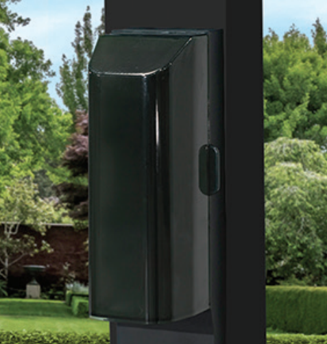 Black wall-mounted outdoor device on a dark post, with greenery in the background