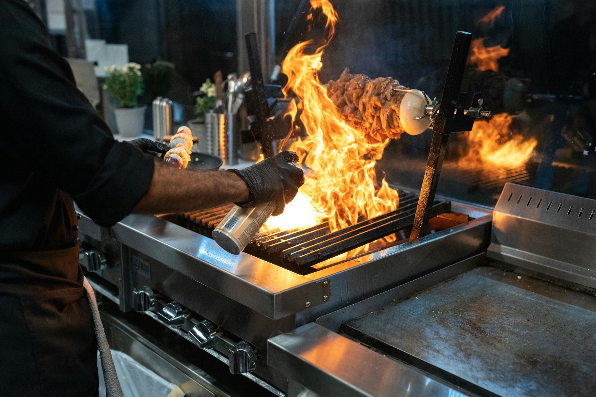 Cook tending a blazing grill with flames rising over stainless steel in a kitchen