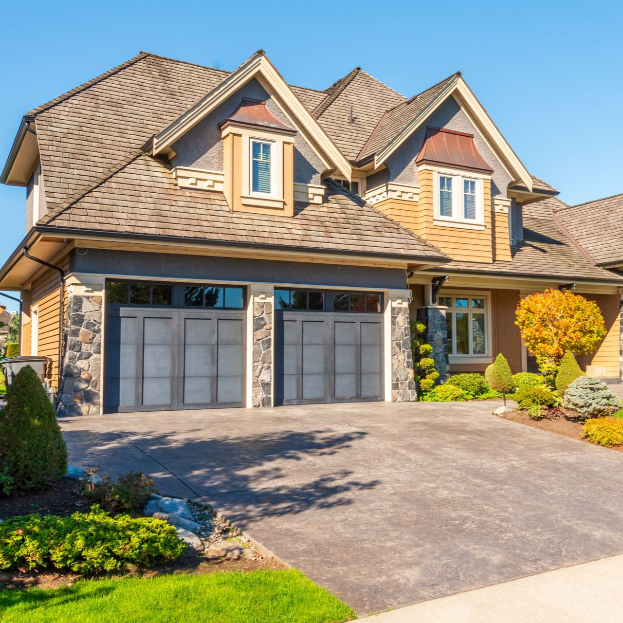 Two-story suburban house with beige siding, stone accents, and a double garage in bright sunlight