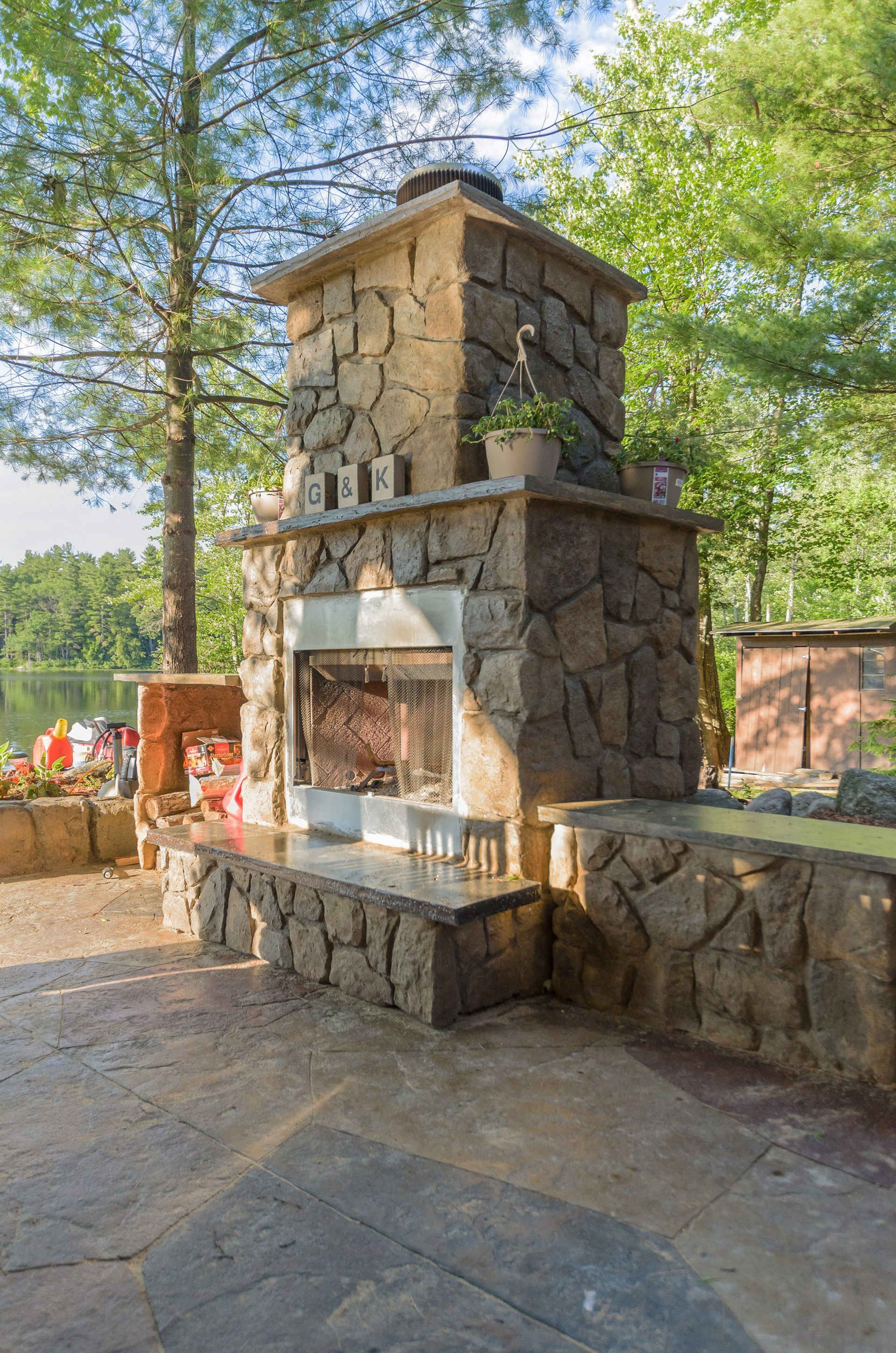 A large stone fireplace is sitting on top of a patio next to a lake.