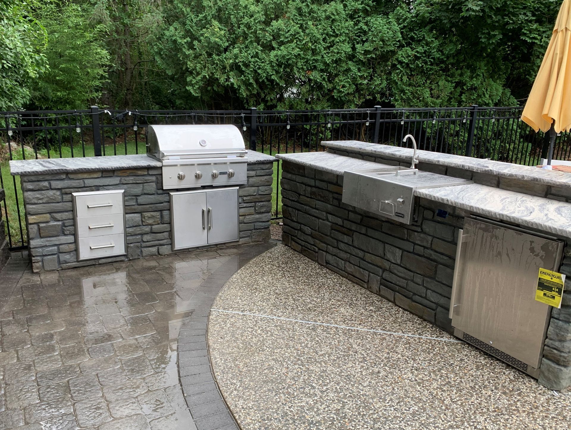 Outdoor stone patio with built-in grill, sink, and countertop beside a wet curved walkway
