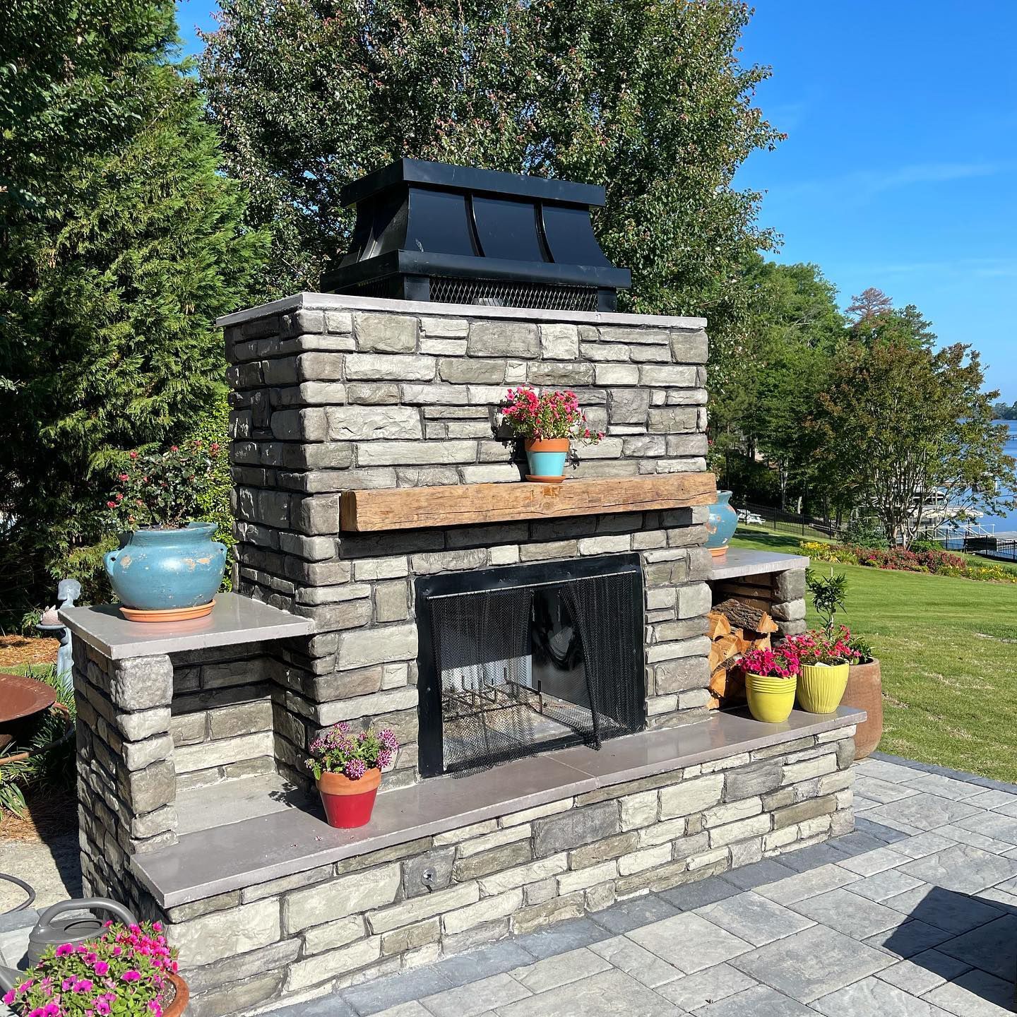 Stone outdoor fireplace with flower pots on a sunny patio