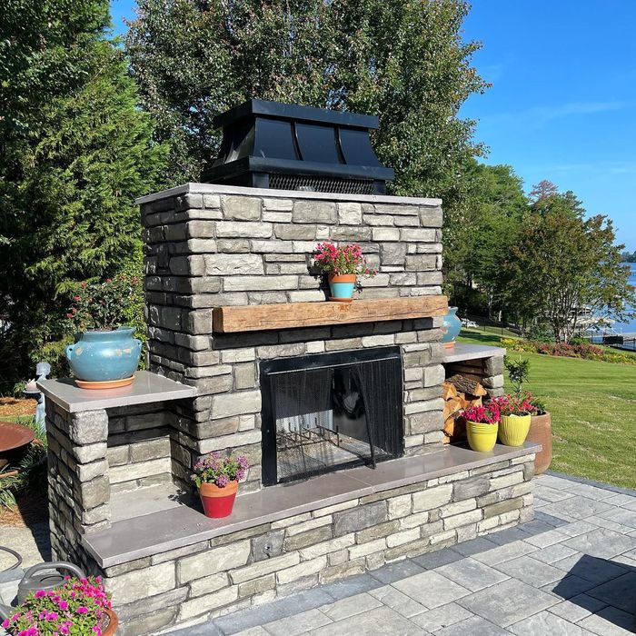 A brick fireplace with flowers and potted plants on a patio.