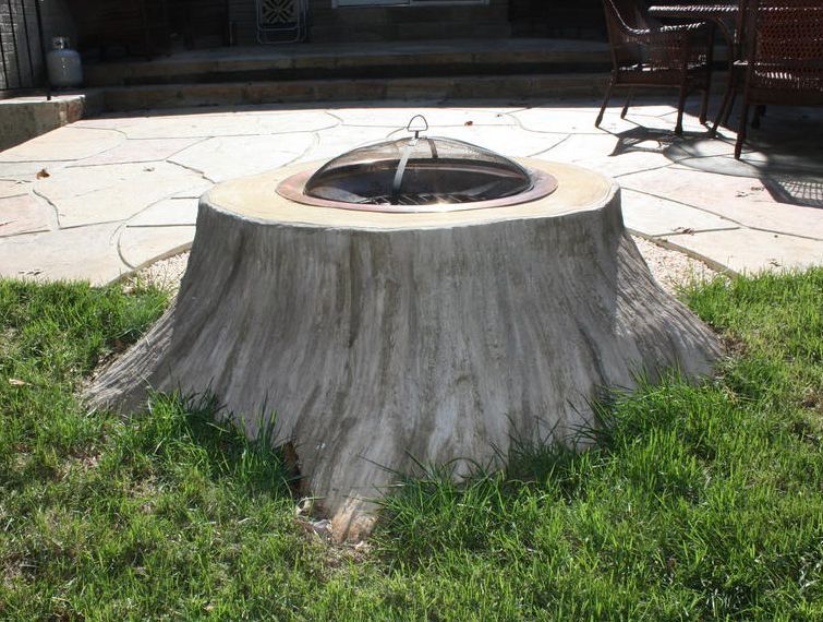 Tree stump-shaped fire pit in a grassy yard with a metal cover on top