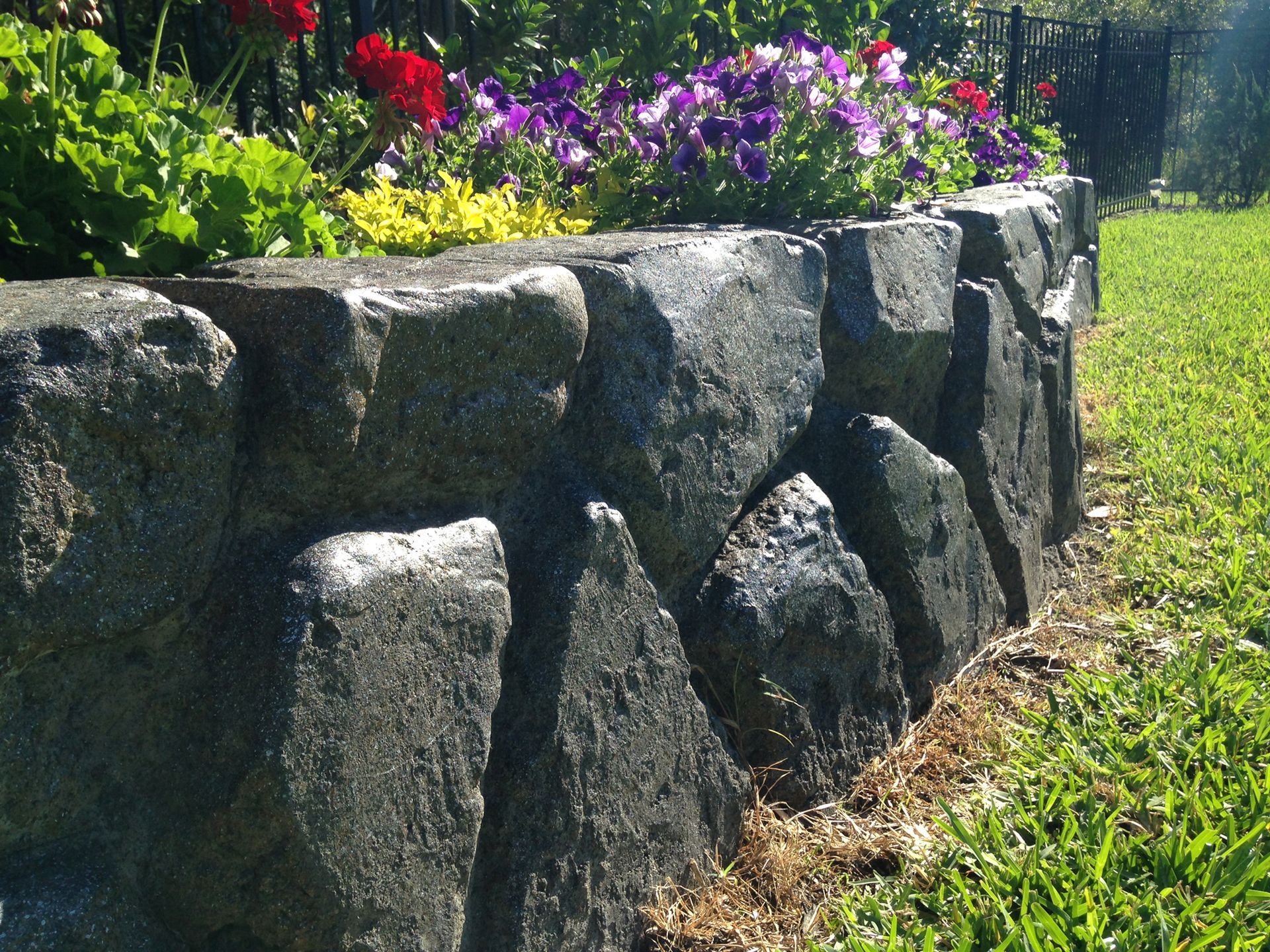 Stone garden retaining wall with colorful flowers and green grass on top