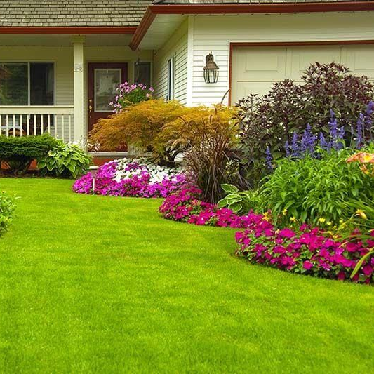 Front yard with bright green lawn and colorful flower beds beside a house porch
