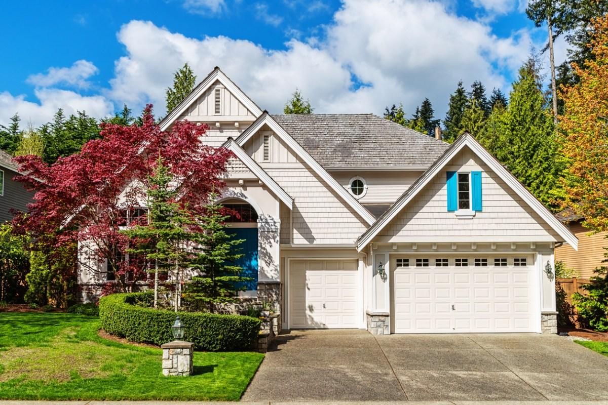 Suburban house with white siding, gray roof, blue shutters, and a red maple tree in front