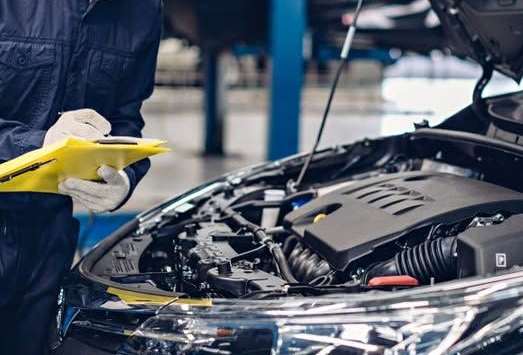 Mechanic inspecting a car engine with the hood open in a repair shop