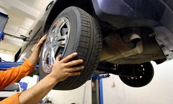 A man is changing a tire on a car on a lift.