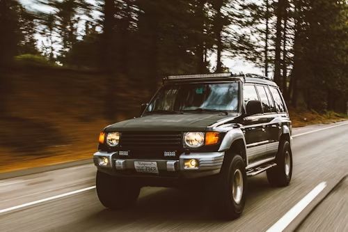 Dark green SUV driving on a road through a forest.
