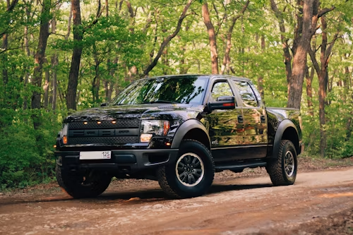 Black pickup truck parked on a dirt road in a green forest