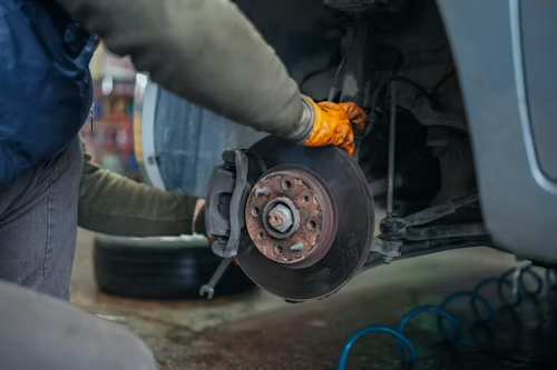 Mechanic removing a car wheel in a garage, with the brake rotor and caliper exposed.