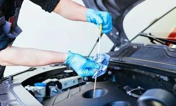 Mechanic in blue gloves checking car engine oil dipstick in a garage.