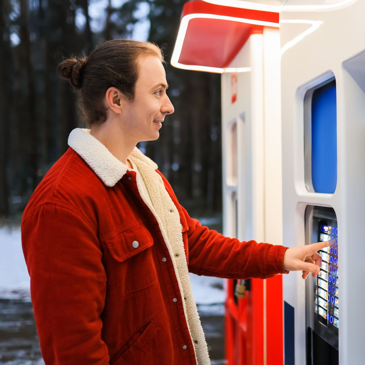Une personne portant une veste rouge utilise un kiosque ou un terminal de paiement à l'extérieur en hiver