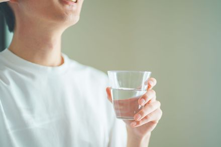 Personne en chemise blanche tenant un verre d'eau sur fond vert tendre