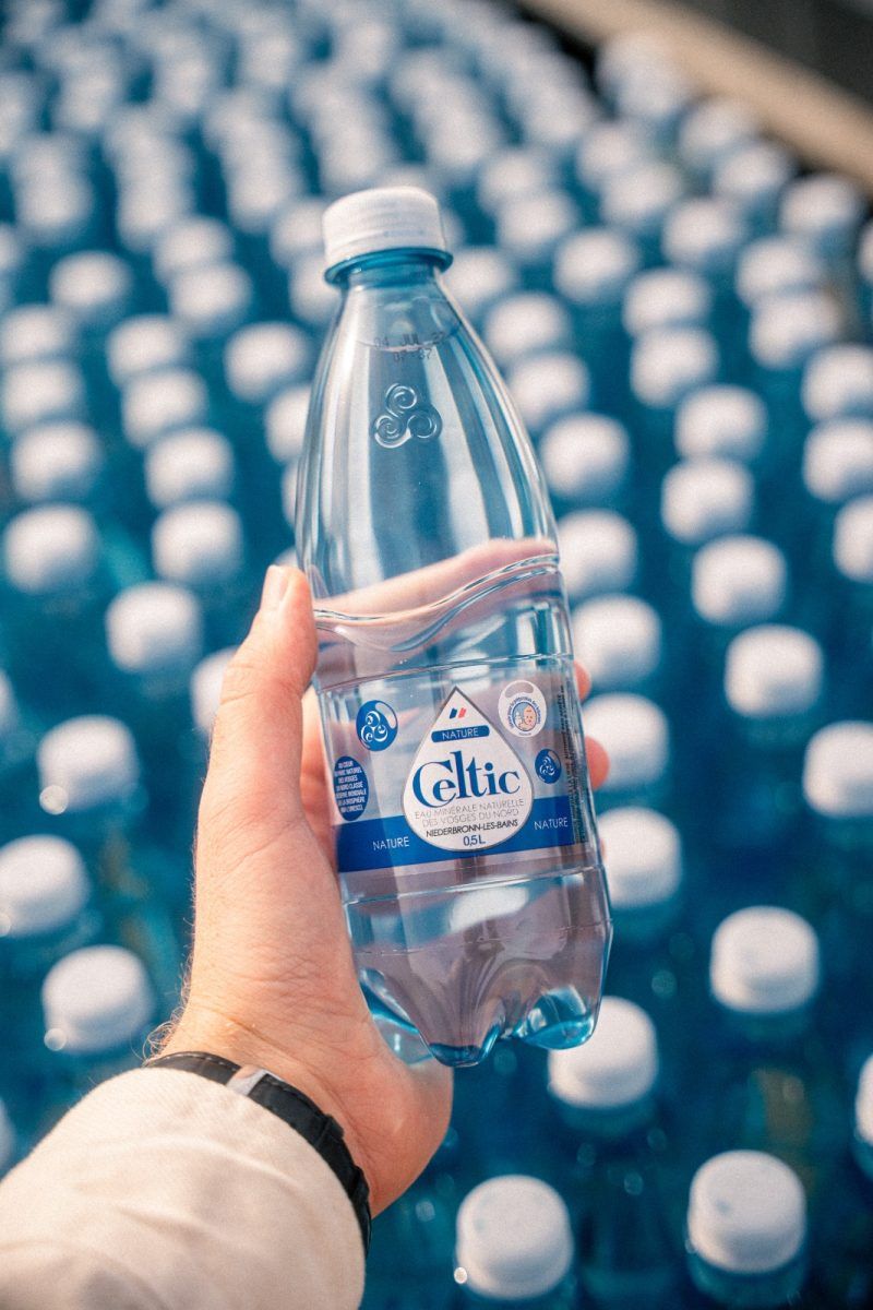 Une main tenant une bouteille d'eau Evian sur un fond flou de nombreuses bouteilles d'eau
