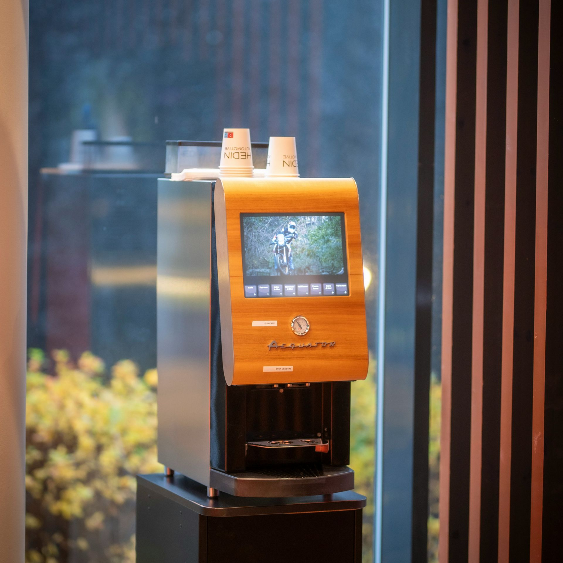 Distributeur automatique orange avec écran tactile et deux gobelets sur le dessus, dans un environnement intérieur moderne
