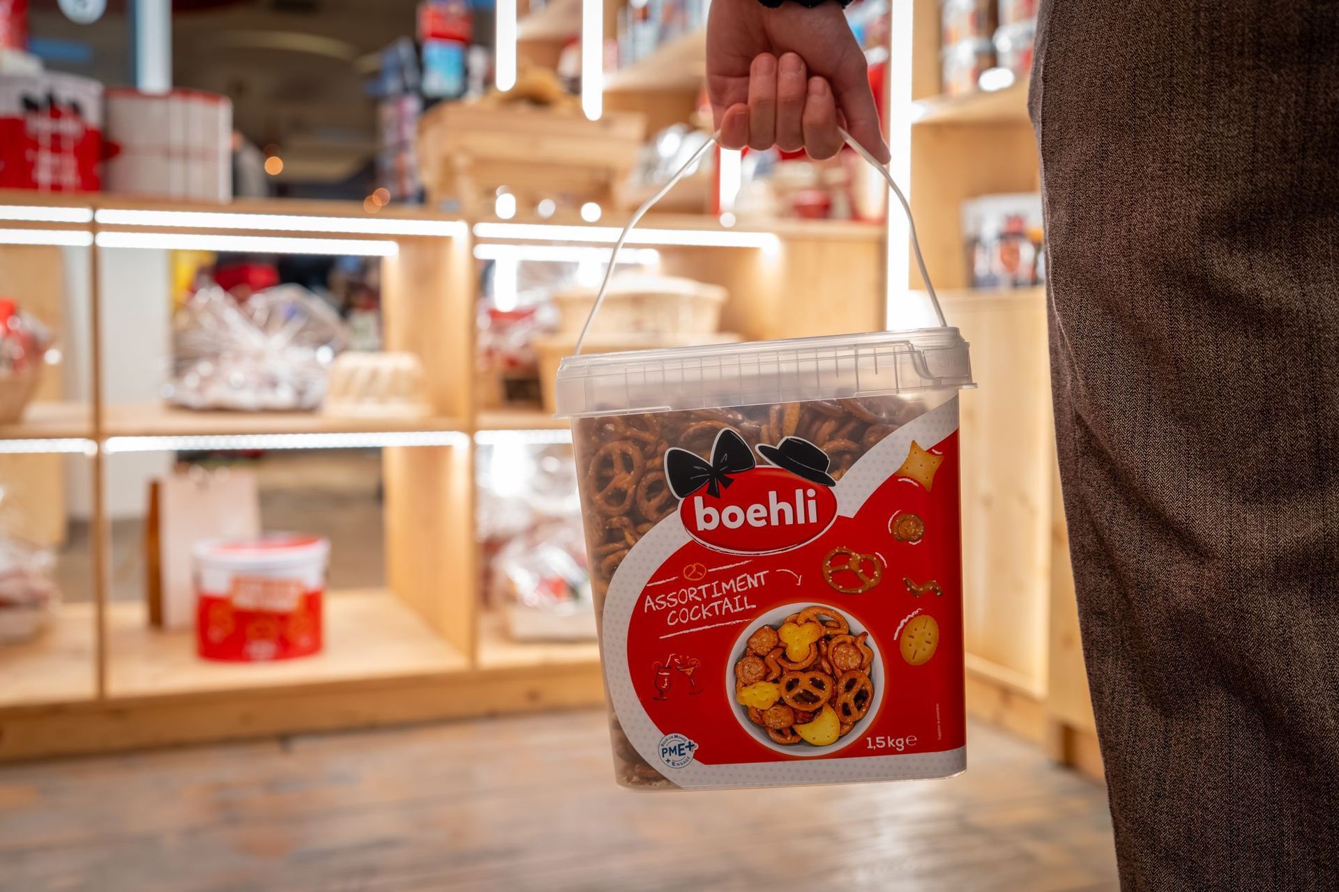 Une main tenant un sachet de snacks Boshil rouge dans une allée de magasin, avec des étagères en arrière-plan.