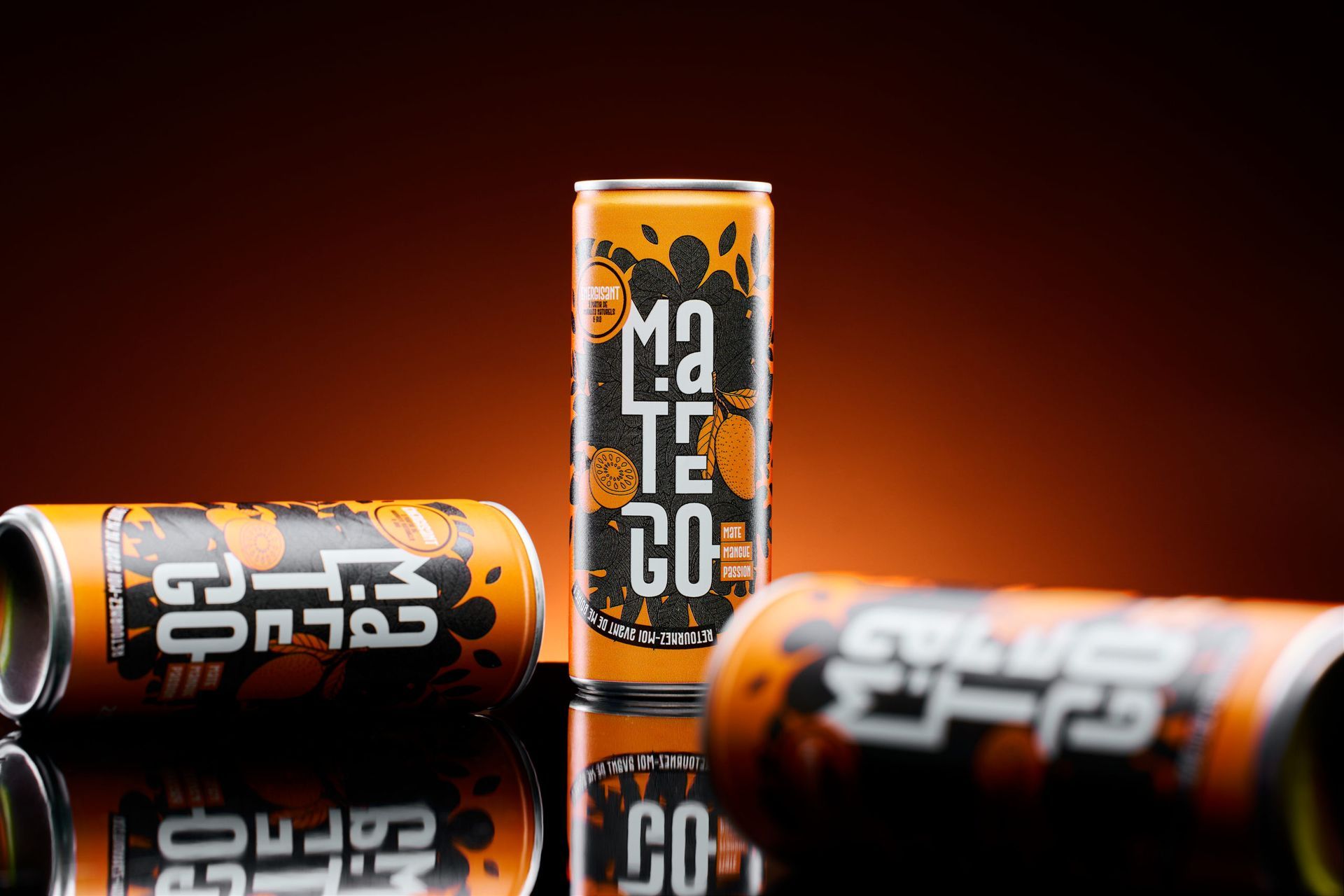Trois canettes de boisson énergisante MaTenGo orange et noire sur fond rouge foncé
