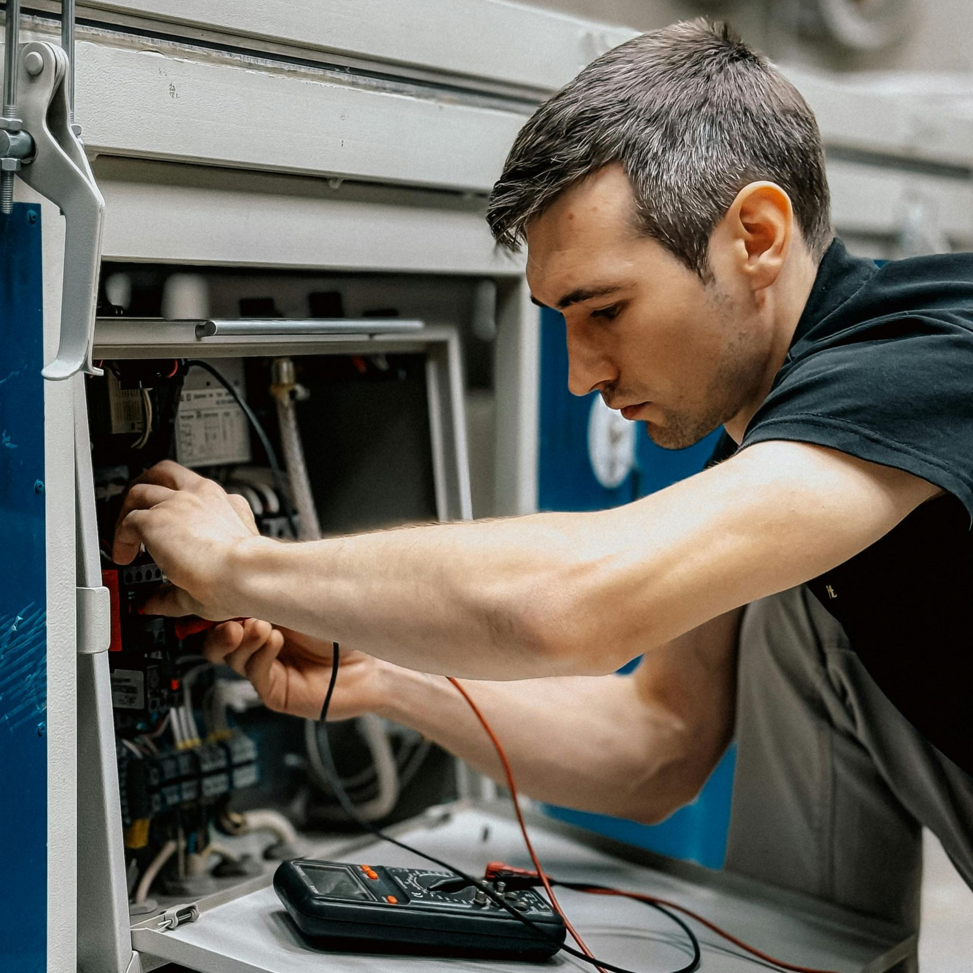 Un technicien teste le câblage d'une machine à l'aide d'un multimètre dans un espace de travail industriel.