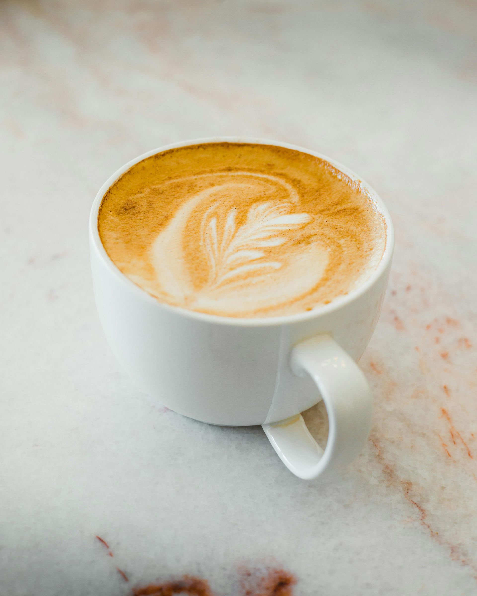 Latte servi dans une tasse blanche à motif de feuilles sur fond marbré.