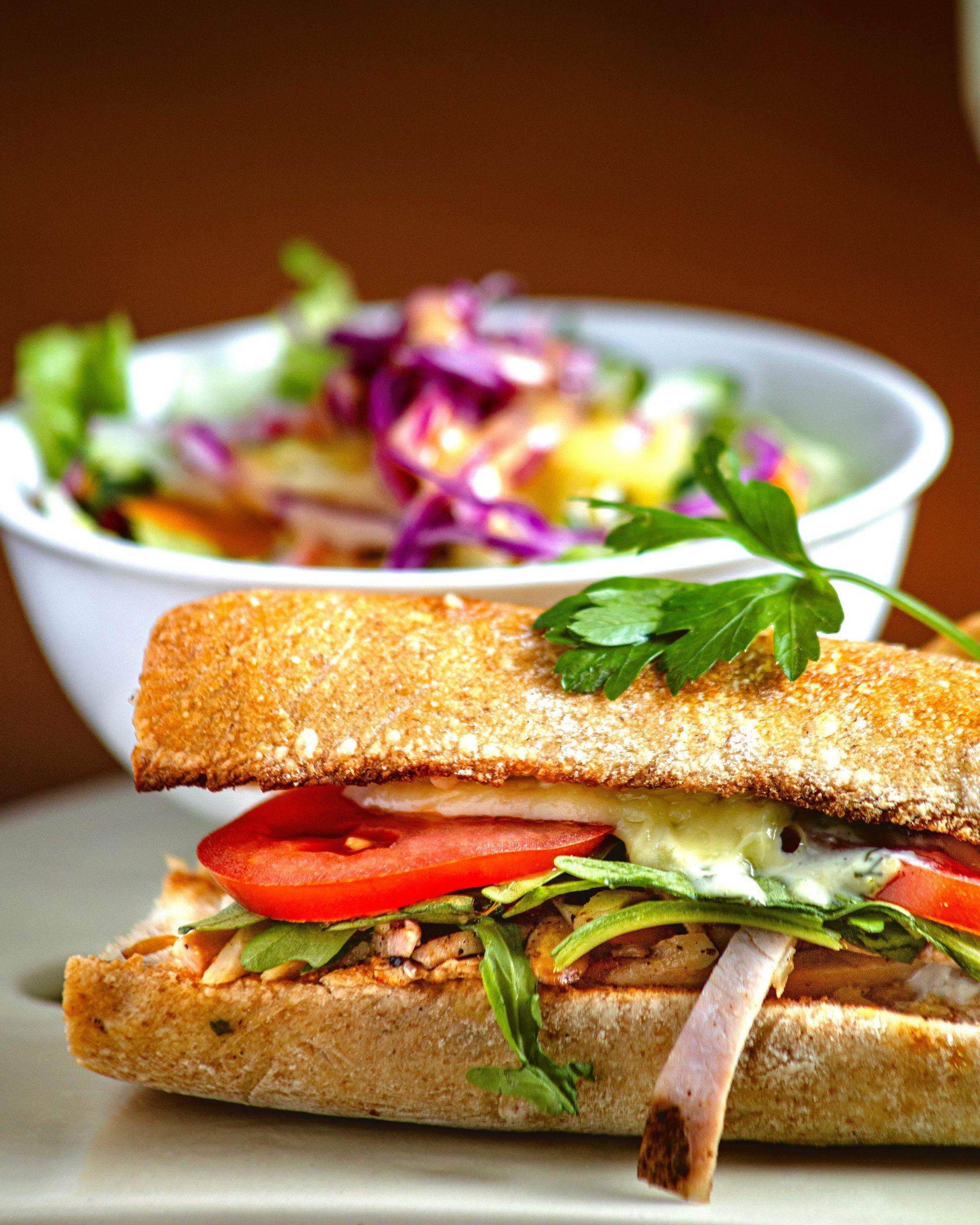 Sandwich à la tomate et à la salade verte devant un saladier coloré