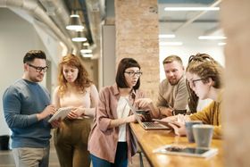 Un groupe de personnes dans un bureau, regardant un ordinateur portable et une tablette, discutant d'un projet.